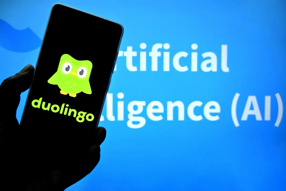 Logo Duolingo trên điện thoại với nền chữ "Artificial Intelligence (AI)" phía sau.